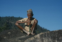 Nepal, Bumlingtar, Old man sitting on rock carving with knife.