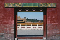 China, Beijing, Imperial Palace, View through archway in red bricked wall toward rooftops and terrace.