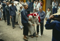 China, Guangxi Province, Fuli, Chief mourner in funeral procession being supported along street watched by crowds.