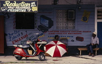 Guyana, Georgetown, Snack vendor in front of building advertising electrical equipment and reduced Indian and English music recordings on tape cassette.