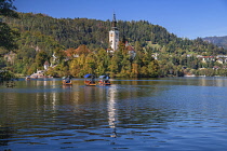 Slovenia, Upper Carniola, Bled, Gondola Pletnas on Lake Bled ferrying tourists to Bled Island with the tower of the Church of the Annunciation visible in the background.