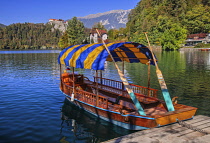 Slovenia, Upper Carniola, Bled, Gondola Pletna on shore of Lake Bled awaiting tourists with Bled Castle visible in the background.