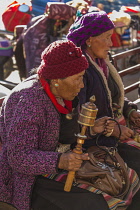 An older Tibetan woman spins her prayer wheel while holding her mala rosary beads in Lhasa, Tibet.