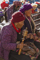 An older Tibetan woman spins her prayer wheel while holding her mala rosary beads in Lhasa, Tibet.