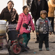 Tibetan children playing on the street by their mother's soup stand in a neighborhood in Lhasa, Tibet.