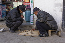 Tibetan men playing checkers on the sidewalk in a neighborhood in Lhasa, Tibet.