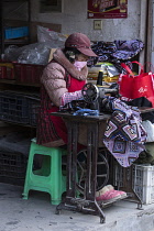 A Tibetan seamstress sews with a foot-treadle sewing machine in front of her shop in a neighborhood in Lhasa, Tibet.