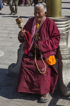 A Tibetan Buddhist nun with her prayer wheel takes a rest while circumambulating  the Potala Palace in Lhasa, Tibet.