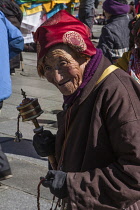 An older Tibetan woman pilgrim circumambulates the Jokhang Temple with her prayer wheel in Lhasa, Tibet.