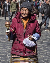An older Tibetan woman pilgrim circumambulates the Jokhang Temple with her prayer wheel in Lhasa, Tibet.  She is wearing her traditional colorful pangden or bangdian apron.