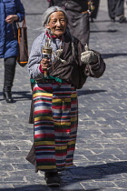 An older Tibetan woman pilgrim circumambulates the Jokhang Temple with her prayer wheel in Lhasa, Tibet.  She is wearing her traditional colorful pangden or bangdian apron.