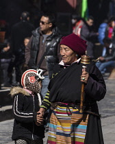 A Tibetan grandmother and her grandchild circumambulate the Jokhang Temple in Lhasa, Tibet with her prayer wheel.