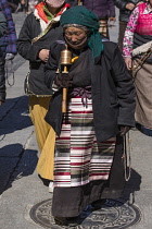 An older Tibetan woman pilgrim circumambulates the Jokhang Temple with her mala rosary beads in Lhasa, Tibet.  She is wearing her traditional colorful pangden or bangdian apron.