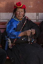 A Tibetan woman in her heavy chuba or chupa sheepskin-lined coat holds her mala rosary beads while on a pilgrimage in Lhasa, Tibet.