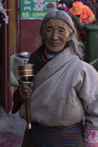 An older Tibetan woman pilgrim circumambulates the Jokhang Temple with her prayer wheel in Lhasa, Tibet.  She is wearing her traditional colorful pangden or bangdian apron.