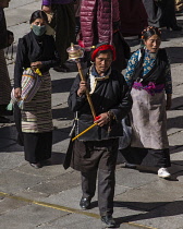 Tibetan Buddhist pilgrims from the Kham region of eastern Tibet circumambulating around the Jokhang Temple in Lhasa, Tibet.  A Khamba man with his red headdress leads his family with a prayer wheel.