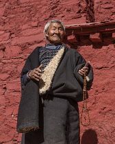 A Tibetan Buddhist pilgrim from the Kham region of eastern Tibet at the Drepung Monastery near Lhasa, Tibet.  He is wearing the heaving sheepskin-lined chuba or chupa coat and is carrying his mala ros...