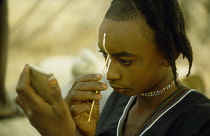 Nigeria, General, Wodaabe tribesman applying face paint using piece of straw.