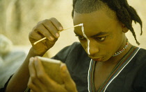 Nigeria, North, General, Wodaabe tribesman applying traditonal face decoration before dance.