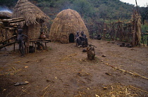 Ethiopia, General, Mursi settlement with woman and children outside thatched huts.