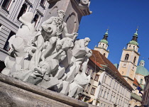 Slovenia, Ljubljana, Close up detail of the figures on the Robba Fountain with towers and dome of the Cathedral of St Nicholas in the background.