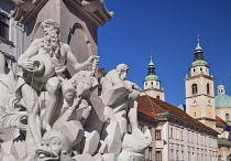 Slovenia, Ljubljana, Close up detail of the figures on the Robba Fountain with towers and dome of the Cathedral of St Nicholas in the background.