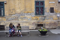 Romania, Timis, Timisoara, Children sitting on street bench, old townl.