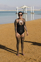 Israel, Ein Bokek, Dead Sea, A young woman enjoys a mud bath treatment on the shore of the Dead Sea at the resort of Ein Bokek in Israel.