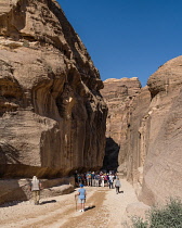 Jordan, Petra, Tourists begin the hike into a narrow slot canyon called the Siq to see the ruins of the Nabataean city of Petra in the Petra Archeological Park is a Jordanian National Park and a UNESCO World Heritage Site. Over their heads at left is the remnant of the stone arch that previously marked the entrance to the Siq.