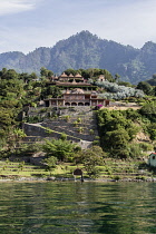 Guatemala, Solola, Lake Atitlan, Spacious villa on the shore with a steep, forested hill behind and lake in foreground.