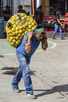 Guatemala, Solola Department, Santiago Atitlan, A young man carries a heavy load of oranges from the market on his back using a tumpline.