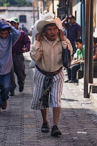 Guatemala, Solola Department, Santiago Atitlan,An older man in traditional dress carries a heavy load  on his back using a tumpline around his forehead.