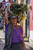 Guatemala, Solola Department, Santiago Atitlan, A Mayan woman wearing traditional dress carries bundles of flowers on her head in the market.