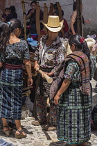 Guatemala, El Quiche Department, Chichicastenango, A  Mayan man in the distinctive outfit from Solola in the Indian market, including a heavy wool rodillera around his waist.  He is buying a new woode...