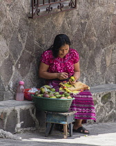 Guatemala, Solola Department, San Pedro la Laguna, A Mayan woman peels mangos on a street curb.