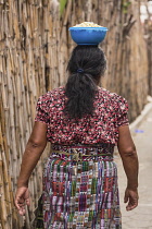 Guatemala, Solola Department, San Pedro la Laguna, A Mayan woman walks along a bamboo fencea with a bowl balanced on her head.