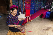 Guatemala, Solola Department, Santa Catarina Palopo, An older Cakchiquel Mayan woman weaves fabric on a backstrap loom while kneeling on the floor of her home.