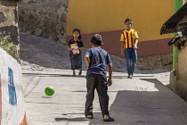 Guatemala, Solola Department, Santa Cruz la Laguna, Two young boys play soccer or football in the street as a girl in traditional dress walks by.