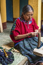 Guatemala, Solola Department, Santa Cruz la Laguna, An older Mayan woman in traditional dress winds thread in preparation for weaving on a back loom.