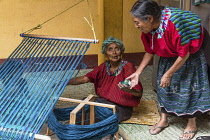 Guatemala, Solola Department, Santa Cruz la Laguna, An older Cakchiquel Mayan woman in traditional dress winds thread on a frame to prepare for weaving on a back loom as her friend comes over to help...
