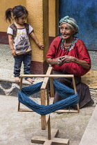 Guatemala, Solola Department, Santa Cruz la Laguna, An older Cakchiquel Mayan woman in traditional dress winds thread on a frame to prepare for weaving on a back loom as a little girl watches.