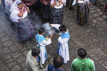 Guatemala, Solola Department, San Pedro la Laguna, Two young altar boys in a religious procession refill the smoking incense burner with more incense resin.