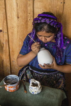 Guatemala, Solola, San Antonio Palopo, A young Mayan woman, wearing typical traditional dress, paints designs on pottery in a workshop.