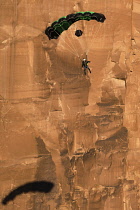 USA, Utah, Moab, A base jumper descends in his parachute off the 400 foot vertical face of the Tombstone in Kane Springs Canyon. Note his shadow on the cliff.