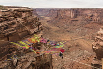 USA, Utah, Moab, A group of slackliners play on the Space Net hundreds of feet above Mineral Canyon during a highline gathering. Behind are several long slacklines over the canyon.