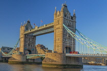 England, London, Tower Bridge in evening light viewed from the south bank of the River Thames with an iconic red London bus crossing the bridge.