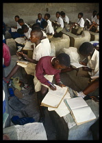 Tanzania, Shinyanga, Uhuru Primary School children working and sitting on large stone blocks as desks.