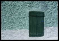 Greece, Peloponese, Tolon, Narrow window with closed green shutters set into pale turquoise and white wall.