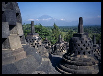 Indonesia, Java, Central, Borobudur Temple ruins.  Buddhist monument constructed in the early 9th century latticed stupas on the upper circular terraces, Mount Merapi in the distance.