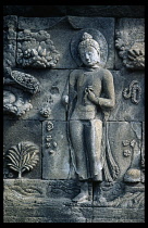 Indonesia, Java, Borobudur, Detail of relief carving on wall of multi tiered Buddhist stupa depicting standing Buddha and flowers.